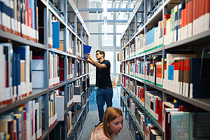 Regale in der Bibliothek Campus Wilhelminenhof mit einer Person bei der Literaturrecherche am Regal